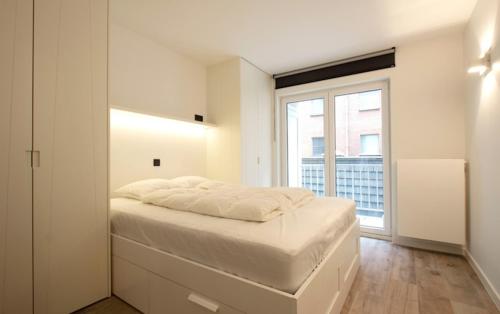 ein weißes Schlafzimmer mit einem großen Bett und einem Fenster in der Unterkunft Riva Bella 1.01 in Nieuwpoort