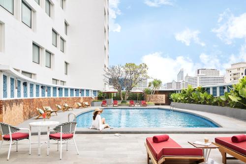 a woman sitting at a table next to a swimming pool at Montien Hotel Surawong Bangkok in Bangkok