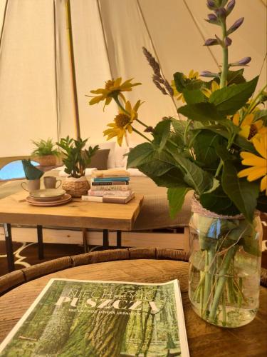 a table with a vase with flowers and a magazine at Puszcza Glamping in Kuraszewo
