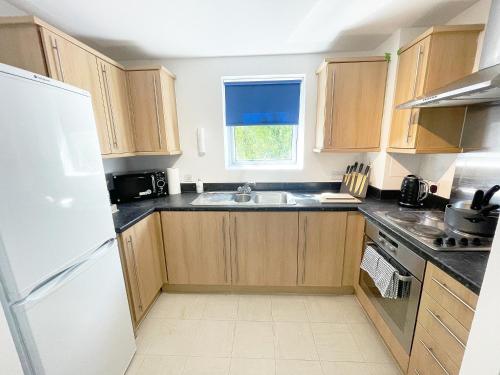 una cucina con armadi in legno e frigorifero bianco di Travaal - 2 Bed Serviced Apartment Farnborough a Farnborough