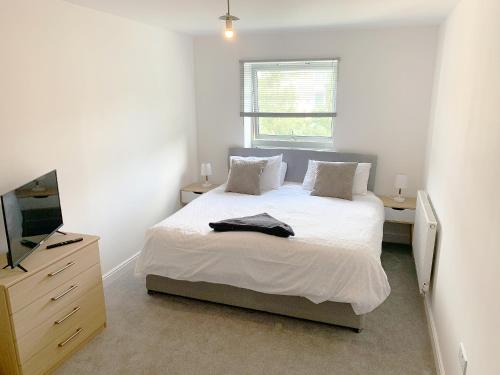 a white bedroom with a bed and a television at Travaal - 2 Bed Serviced Apartment Farnborough in Farnborough