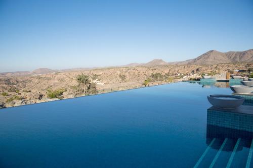 a swimming pool with blue water and mountains in the background at Anantara Al Jabal Al Akhdar Resort in Al ‘Aqar