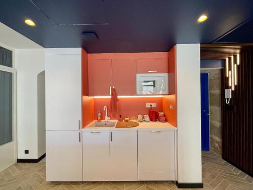 a kitchen with white cabinets and an orange wall at Roma Divine home cinéma et jardin in Nîmes