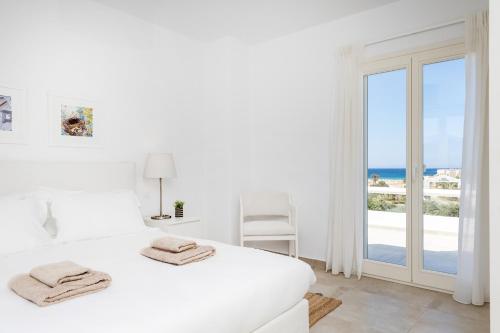 a white bedroom with a bed and a view of the ocean at Naxian Resort in Aliko Beach