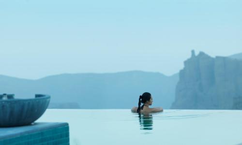 a woman sitting in the infinity pool of a hotel at Anantara Al Jabal Al Akhdar Resort in Al ‘Aqar