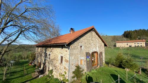 an old stone building with a red roof on a field at Jasserie Les Airelles in Saint-Anthème