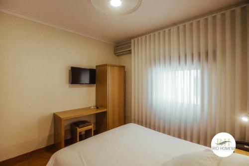 a bedroom with a bed and a television and a window at Rio Homem in Terras de Bouro
