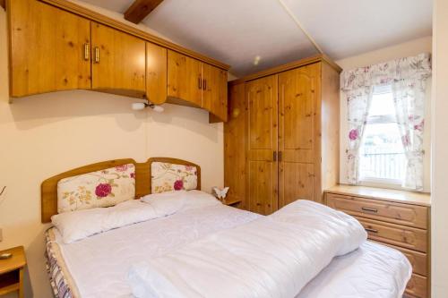 a bedroom with a bed and wooden cabinets and a window at Great Dog Friendly Caravan For Hire At North Denes In Suffolk Ref 40068nd in Lowestoft