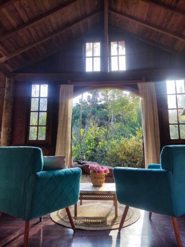 a living room with two blue chairs and a large window at Chalé Candeia no Matutu in Aiuruoca