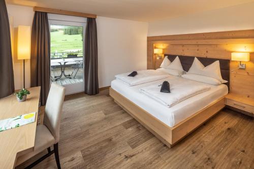 a bedroom with a bed and a desk and a window at Hotel Sella***s in Selva di Val Gardena