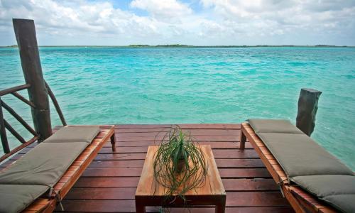 a wooden pier with a table and chairs on the water at Akalki Hotel y Centro Holistico in Bacalar
