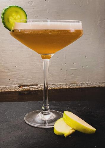 a drink in a martini glass next to a sliced pickle at Castle Hotel in Eynsford