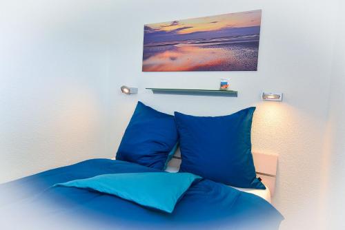 a bed with blue pillows and a painting above it at Am Sahlenburger Strand AS11 in Cuxhaven