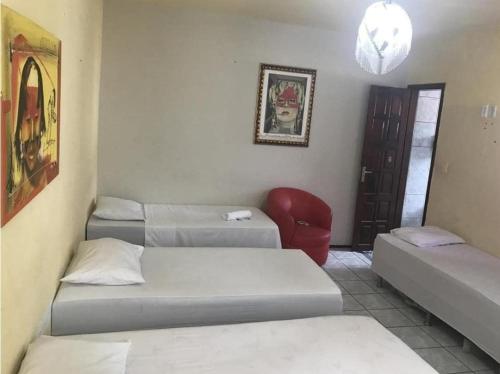 um quarto com três camas e uma cadeira vermelha em pousada Sol e Praia em Fortaleza