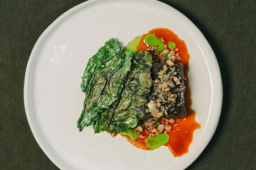 a white plate of food with greens and sauce at Santa Barbara Eco-Beach Resort in Ribeira Grande
