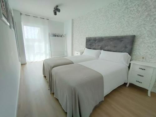 a white bedroom with two beds and a window at Second Home Arzúa apartamentos in Arzúa