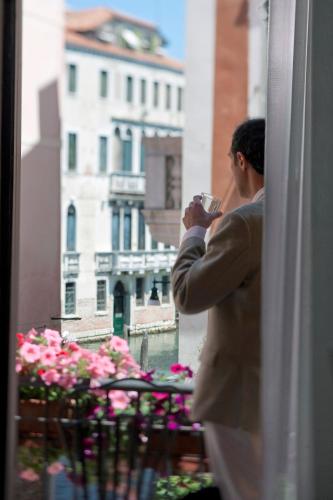 a man in a suit drinking a drink from a window at Hotel Al Malcanton in Venice
