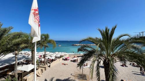 a beach with a flag and palm trees and the ocean at Princess Palace Beach Monte-Carlo in Monte Carlo