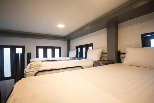 a room with four beds with white sheets and windows at Billabong Hostel in Baan Tai