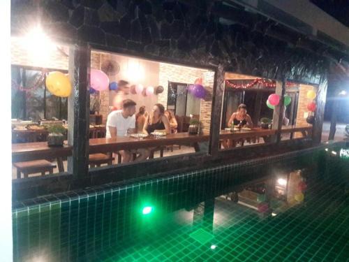 a group of people sitting at a restaurant next to a pool at Billabong Hostel in Baan Tai