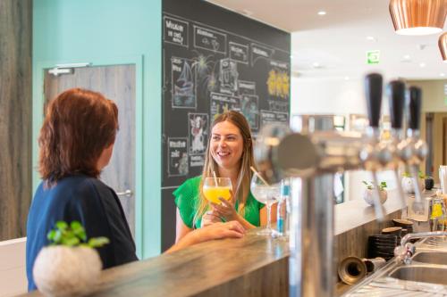 a woman sitting at a bar holding a glass of orange juice at ibis Styles Nieuwpoort in Nieuwpoort