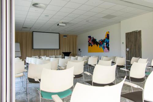 a room with white chairs and a projection screen at ibis Styles Nieuwpoort in Nieuwpoort