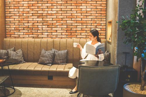 a woman sitting on a couch reading a book at Twin-Line Hotel Karuizawa Japan in Karuizawa