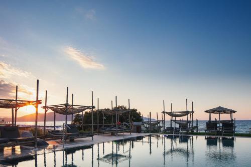 a pool with chairs and umbrellas and the ocean at La Mer Resort Spa Crete in Georgioupolis