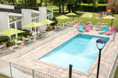 einen Blick über einen Pool mit Stühlen und Sonnenschirmen in der Unterkunft Holiday Inn Lille Ouest Englos, an IHG Hotel in Englos
