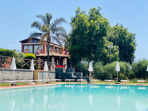 a large swimming pool with umbrellas in front of a house at Agricampeggio Verde Etna in Aci SantʼAntonio