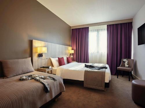 a hotel room with two beds and a chair at Mercure Versailles Paris Ouest in Le Chesnay