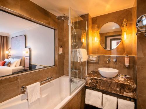 y baño con bañera, lavabo y espejo. en Mercure Versailles Paris Ouest, en Le Chesnay