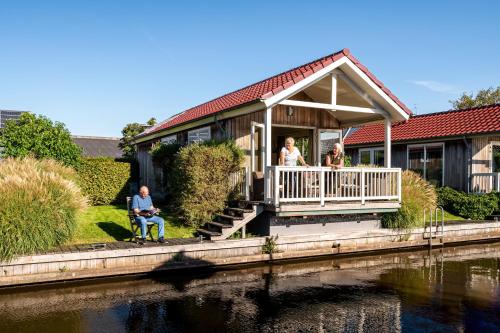 a family sitting on the porch of a house next to a river at Recreatiepark Tusken de Marren in Akkrum