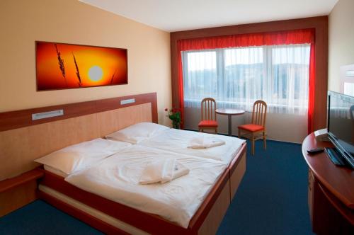 Hotel Lázně Kostelec في زلين: غرفة نوم بسرير ومكتب وتلفزيون