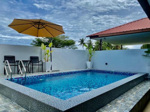 a swimming pool with an umbrella next to a building at ALOR SENARI HOMESTAY PRIVATE POOL in Pantai Cenang