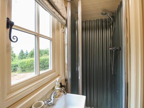 La salle de bains est pourvue d'un lavabo, d'une fenêtre et d'une douche. dans l'établissement High Grounds Shepherd's Hut, à Ashbourne