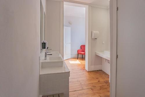 Baño blanco con lavabo y silla roja en Rosalma Hostel, en Oporto