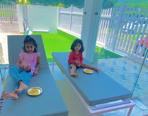 two little girls sitting on benches with plates of food at River Stay - Homestay by Wanderlust Rural Tourism in Dehradun