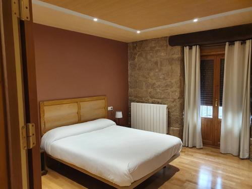 a bedroom with a white bed and a stone wall at Hostal Rural 18 de Abril in Olite