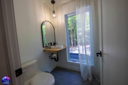 La salle de bains est pourvue de toilettes, d'un lavabo et d'une fenêtre. dans l'établissement Chalet Forestria - SPA- Billard- Ski, à Mansonville