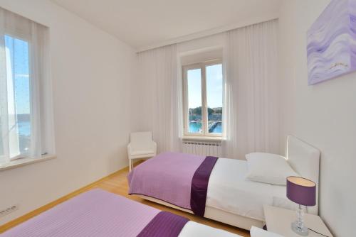 a white bedroom with a bed and two windows at Eden Penthouse Apartments in Zadar