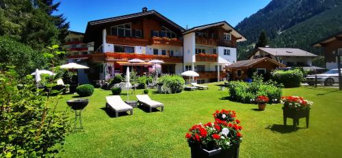 - un grand bâtiment avec une cour agrémentée de chaises et de fleurs dans l'établissement Gästehaus Thaler, à Mittelberg