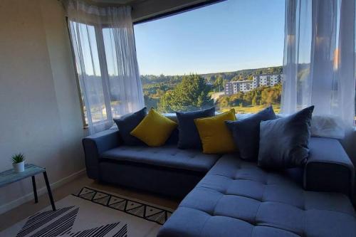 un sofá azul en una sala de estar con una gran ventana en Acogedor Apartamento, rodeado de Naturaleza y Mar., en Puerto Montt