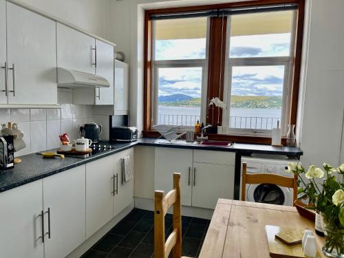 a kitchen with white cabinets and a table and two windows at A Shore Stay in Gourock