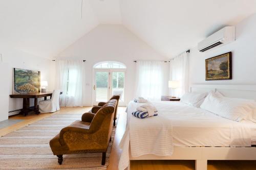 a white bedroom with a large bed and a chair at Sunlit Serenity in West Tisbury