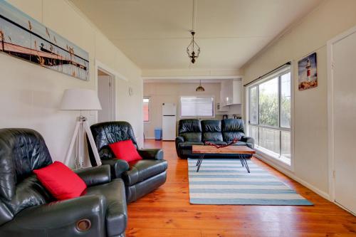 a living room with black leather furniture and red pillows at Wings and Waves in Port Fairy