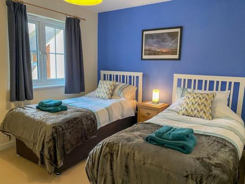 1 dormitorio con 2 camas y pared azul en Dunes Walk Cottage, en Camber