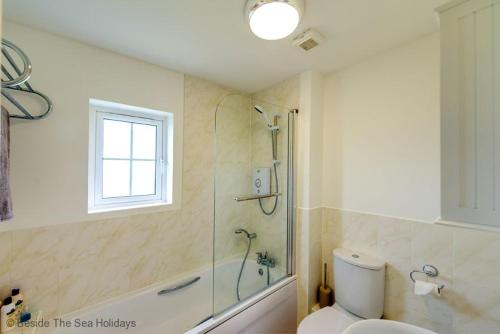 een badkamer met douche en toilet en een raam bij Mallow Cottage in Camber