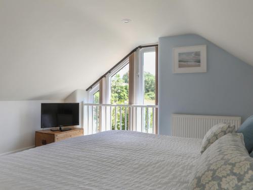 a white bedroom with a bed and a television at Stable End Cottage in Malborough