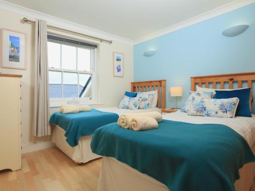 a bedroom with two beds with blue sheets and a window at 8 Thurlestone Beach in Thurlestone